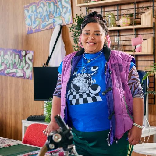 Peggy van Het Kantoor lacht vriendelijk en heeft een knalblauwe trui aan met een paarse bodywarmer