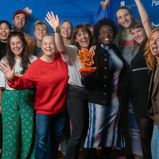 Je ziet een groep juichende mensen met een oranje award in hun hand