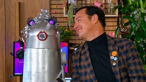 Een man, Luuk, kijkt lachend naar een robot die naast hem staat.