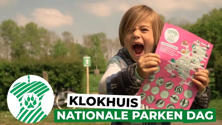 Enthousiast kind houdt roze stempelkaart omhoog tijdens Nationale Parkendag in het groen.
